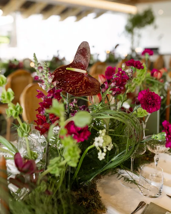 Deep red anthuriums, magenta flowers and greenery on a wedding table, from Nicole’s own wedding.